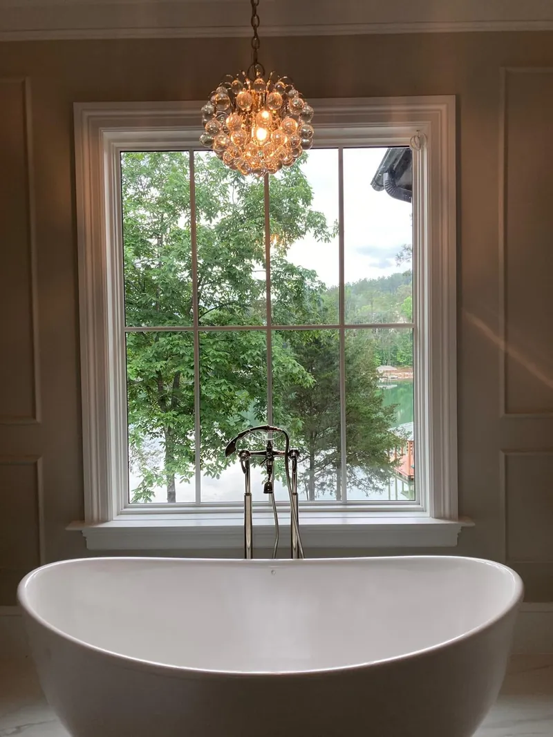 Freestanding bathtub beside a tall window framed by painted walls and trim
