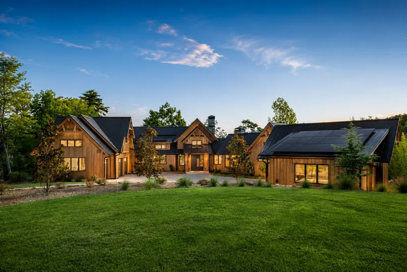 Custom home with natural wood siding, large windows and a lawn at dusk