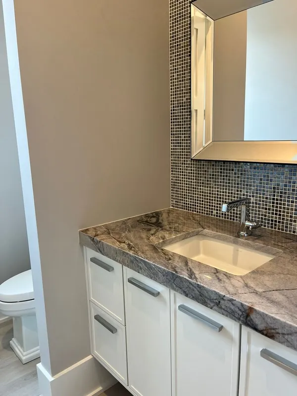 Bathroom vanity with white cabinetry, a stone counter and a tiled backsplash