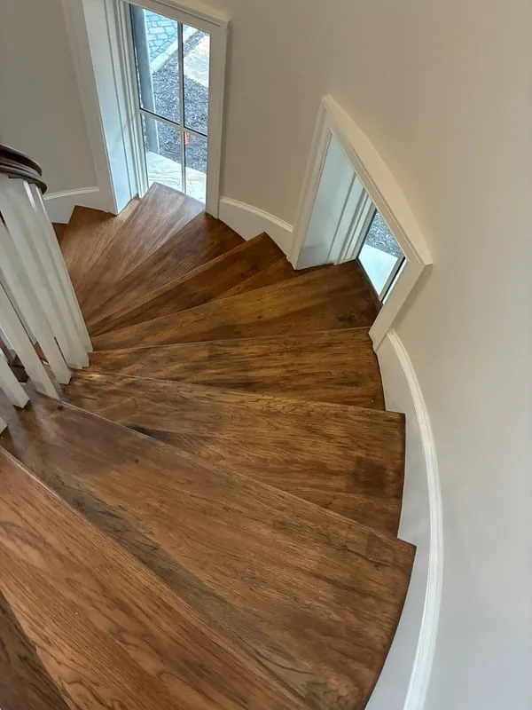 Curved hardwood staircase beside light painted walls and windows