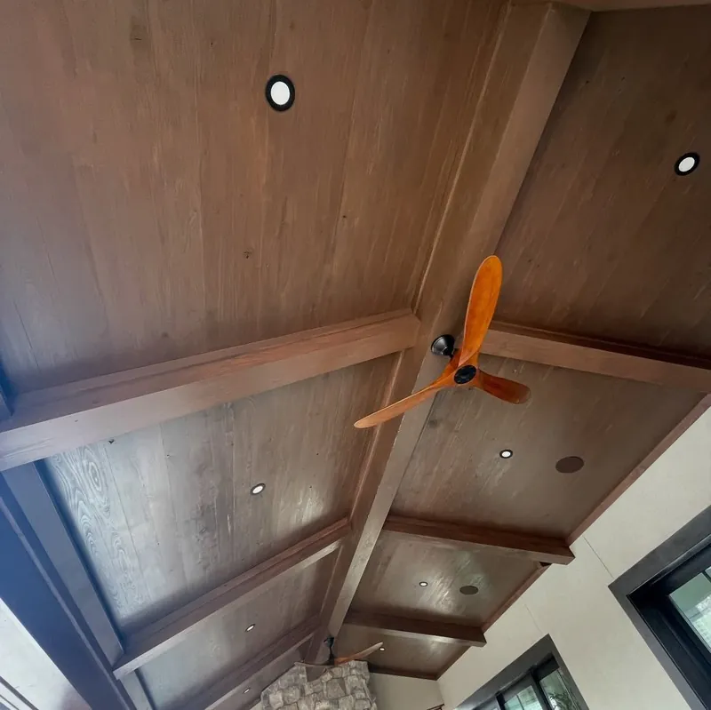 Stained wood ceiling and beams surrounding an orange ceiling fan